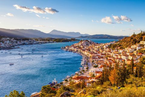 Hills with green spots and trees, blue waters and lovely houses. View of Poros.