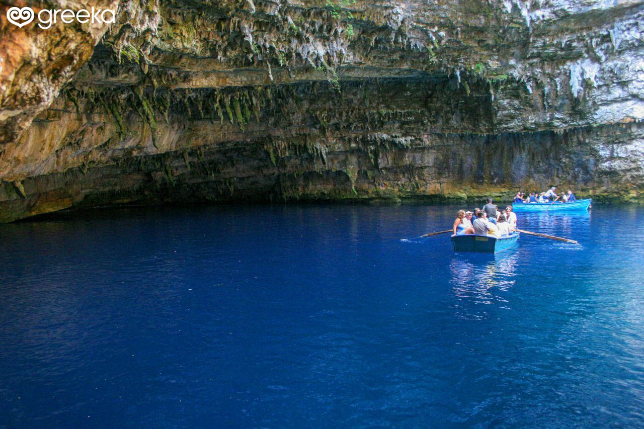 Tour boats cross the deep blue waters of Melissani Cave in Kefalonia while visitors admire the stalactites