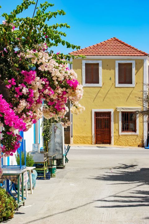 Kattavia: Colorful flowers and a traditional house with wooden shutters and door.