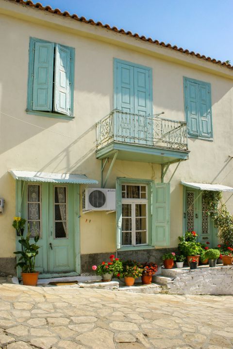 Manolates: A two-floored house with colorful shutters and doors and lovely flower pots.